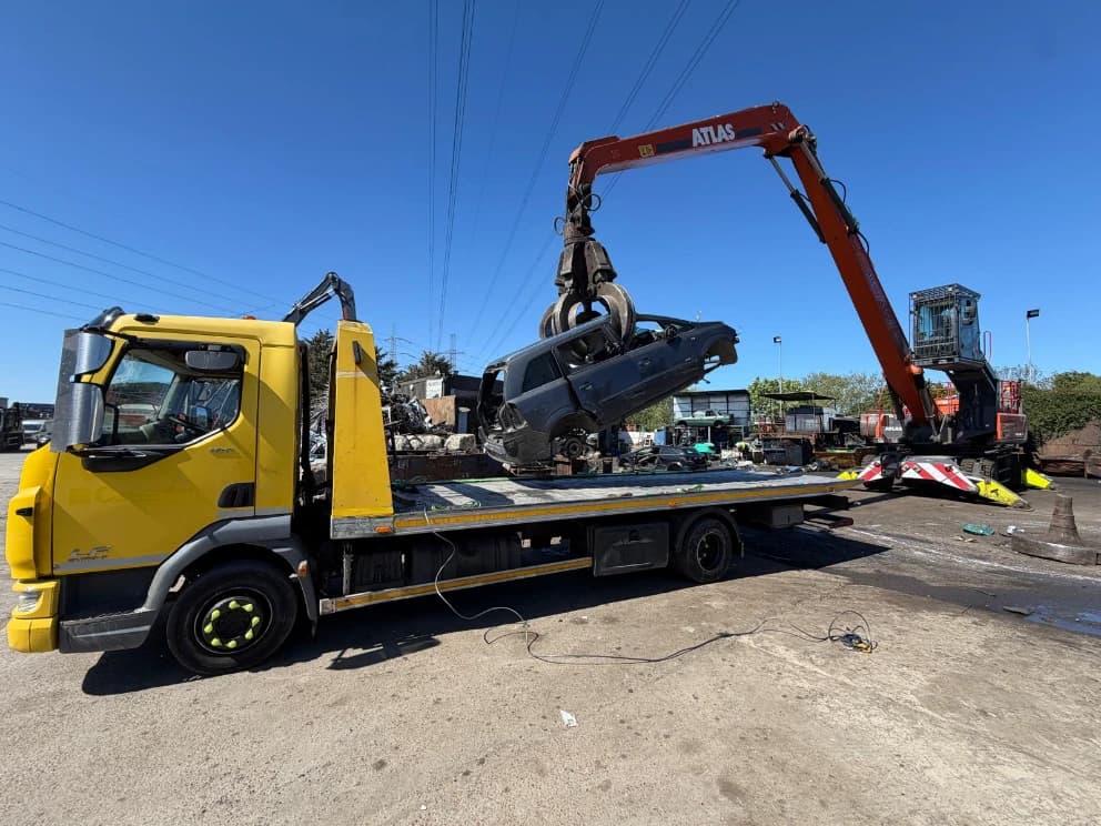Crane loading a crash-damaged vehicle onto a flatbed recovery truck
