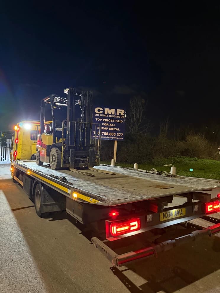 Forklift truck loaded on a flatbed recovery vehicle at night