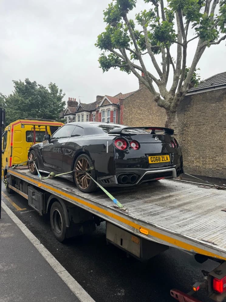 Nissan GT-R loaded on a flatbed recovery truck on a residential street
