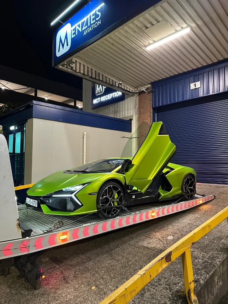 Lamborghini supercar loaded on a flatbed recovery truck outside an airport terminal