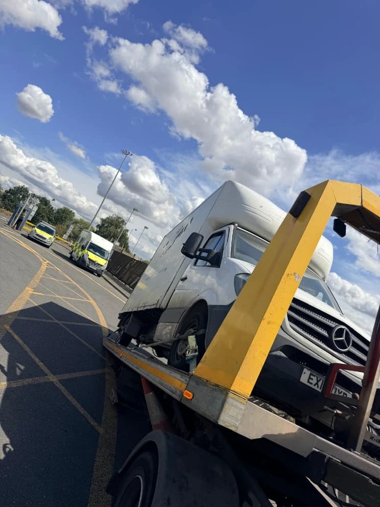 Luton box van loaded on a flatbed recovery truck in a vehicle yard