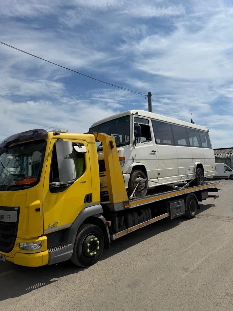 Minibus loaded on a flatbed recovery truck in a vehicle yard