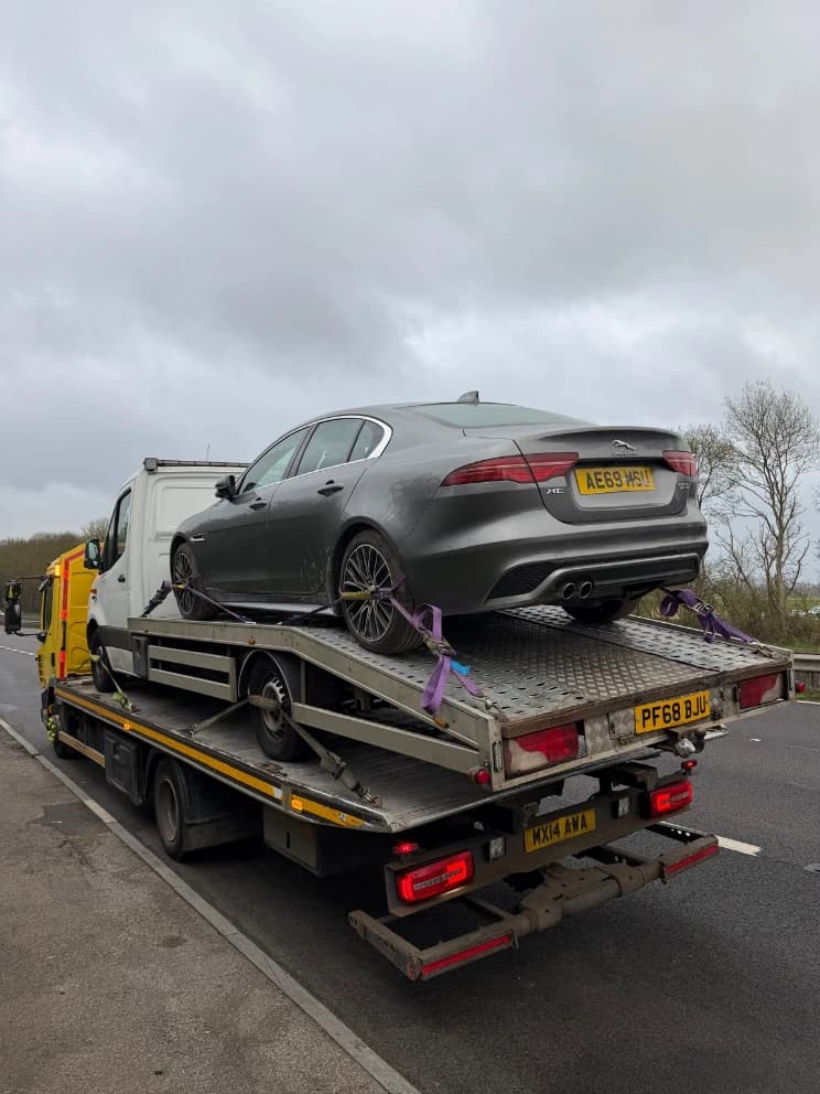 Jaguar XE saloon loaded on a flatbed recovery truck on the motorway hard shoulder