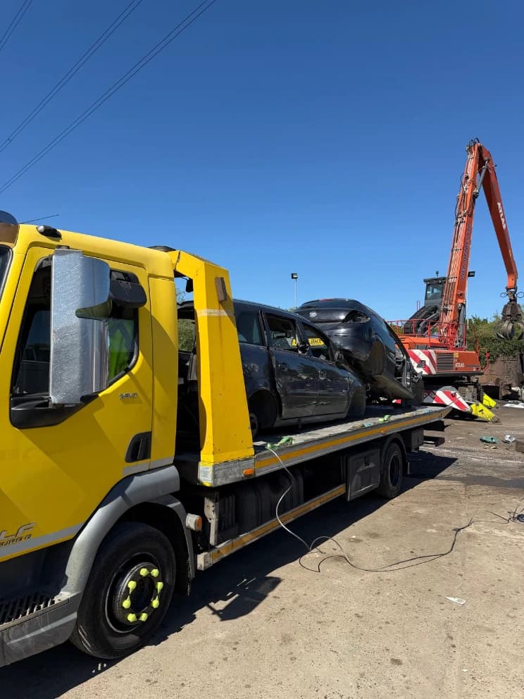 Two crash-damaged vehicles loaded on a flatbed recovery truck at a vehicle recycling yard