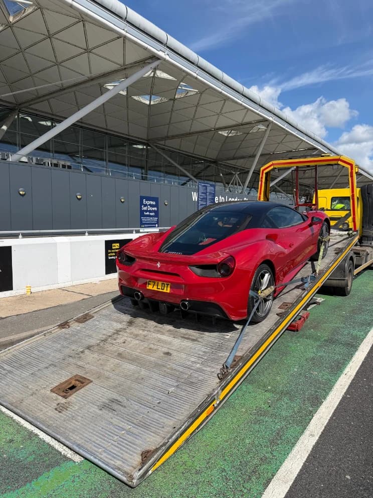 Ferrari sports car loaded on a flatbed recovery truck at an airport