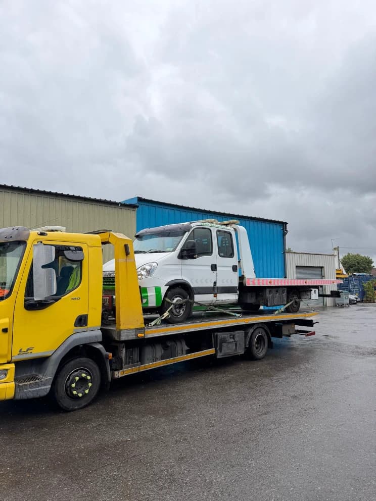 Crew-cab tipper van loaded on a flatbed recovery truck in the rain