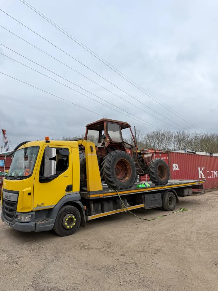 Vintage tractor loaded on a flatbed recovery truck in a yard