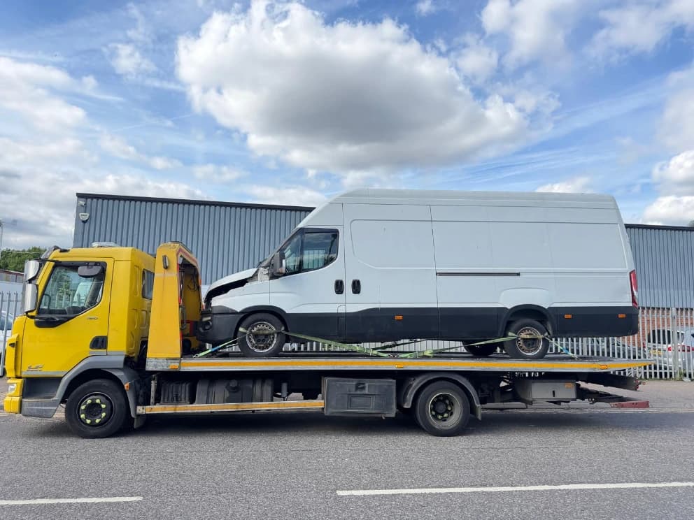Van with front-end collision damage loaded on a flatbed recovery truck