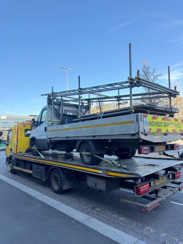AHS Recovery flatbed truck loaded with a highway maintenance vehicle